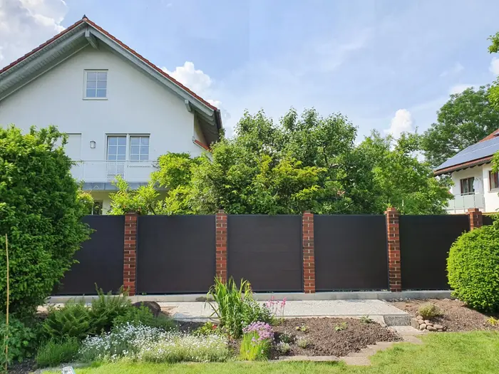 Dunkler Sichtschutzzaun zwischen Klinkerpfeilern vor einem Einfamilienhaus